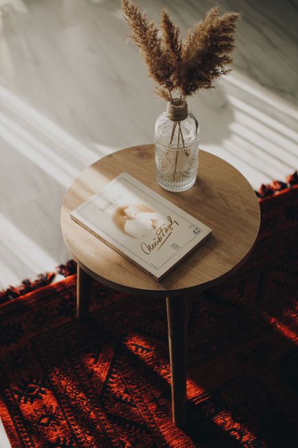 A warm, minimalist living room scene featuring a book and dried grass in a vase on a wooden table.