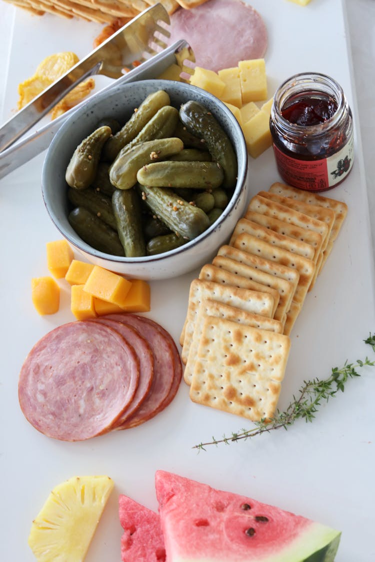 Dill Pickles In A Bowl And Crackers On A White Surface