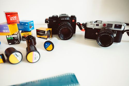 Free Close-up of Leica cameras and assorted film cartridges on a white background, showcasing a classic photography setup. Stock Photo