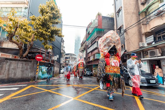 Vibrant parade with costumed figures walking on wet city street under rainy weather.