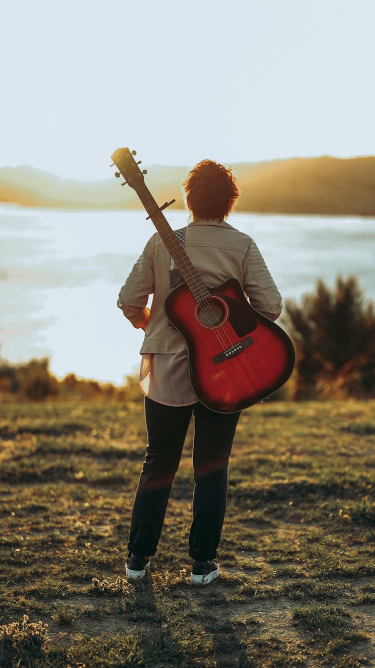 Man With Guitar On His Back Looking Out Into Lake