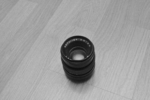Free A Grayscale Photo of a Camera Lens on a Wooden Table Stock Photo