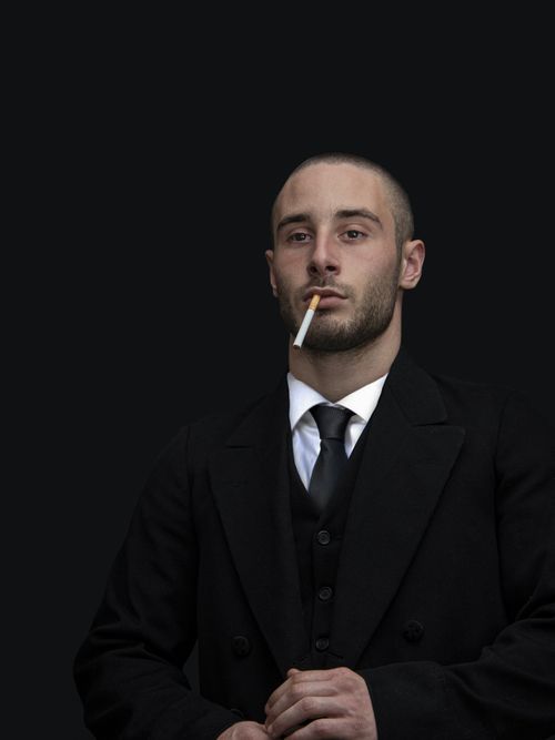 Free A well-dressed man poses seriously with a cigarette, exuding elegance and professionalism. Stock Photo