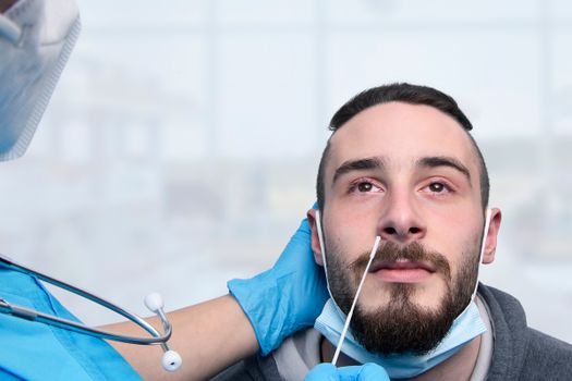 Healthcare professional conducts COVID-19 nasal swab test indoors for bearded adult male.