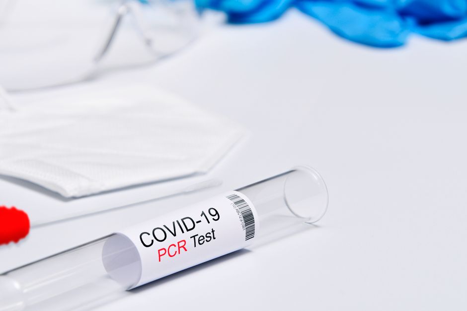 Close-up of a COVID-19 PCR test kit with protective gear on a white surface.