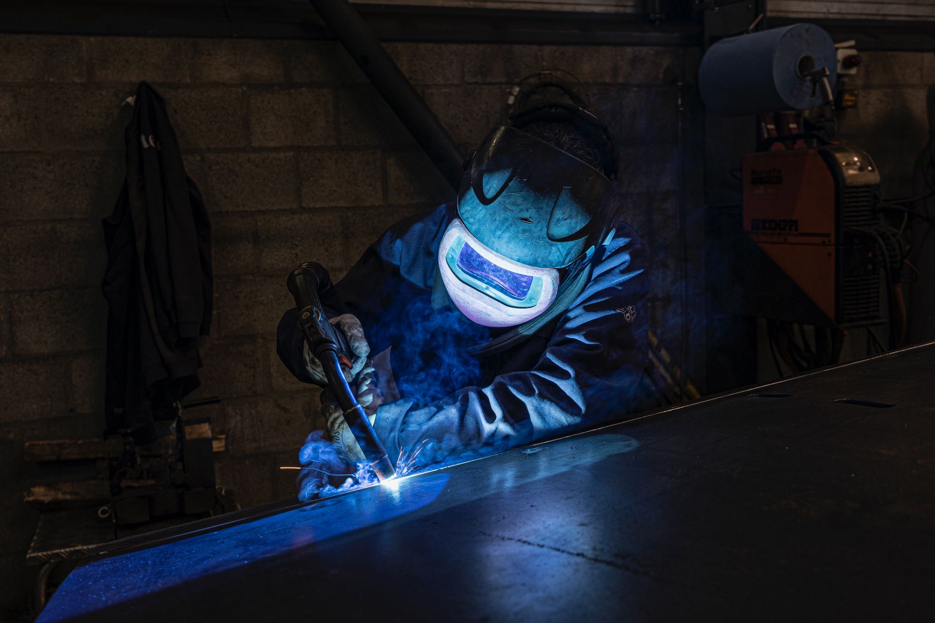 Welder in protective gear working in a workshop, sparks flying.