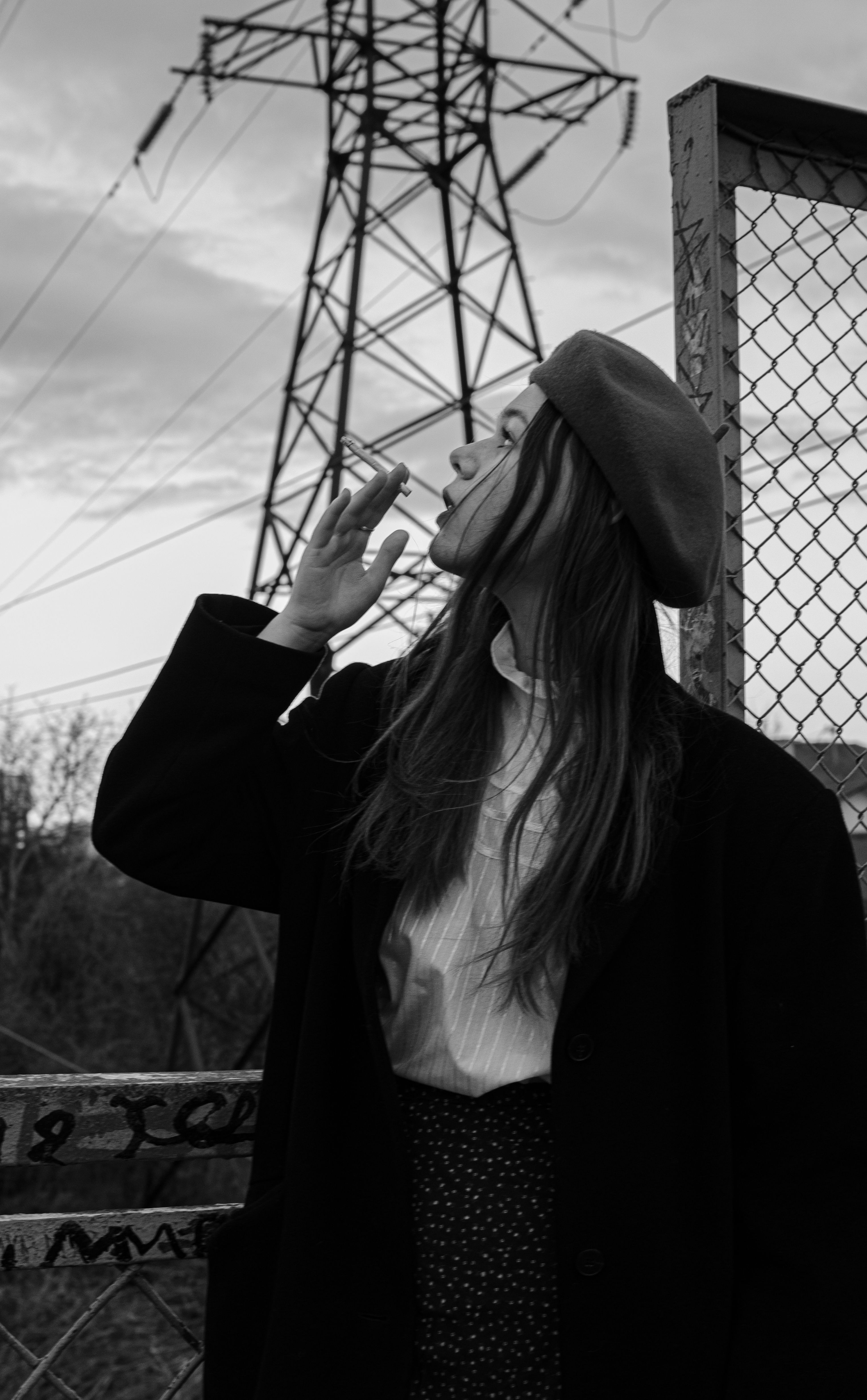 Artistic black-and-white portrait of a woman in a beret, looking thoughtful under power lines.