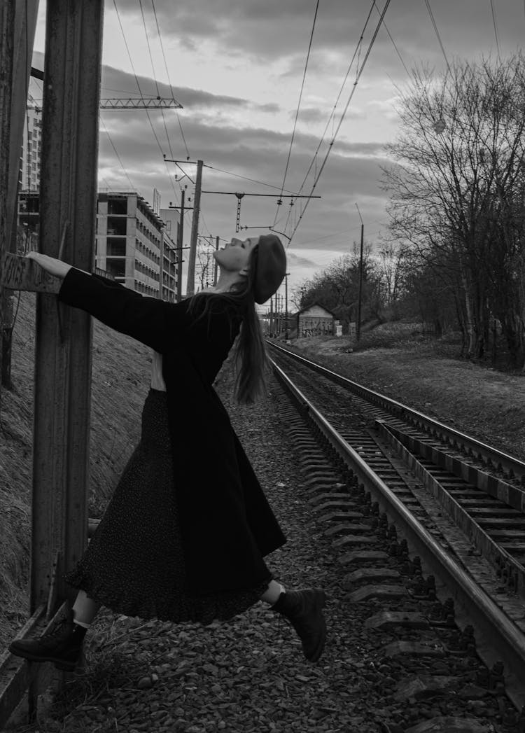 Woman In Black Dress Dancing Around Wooden Pole By Train Tracks