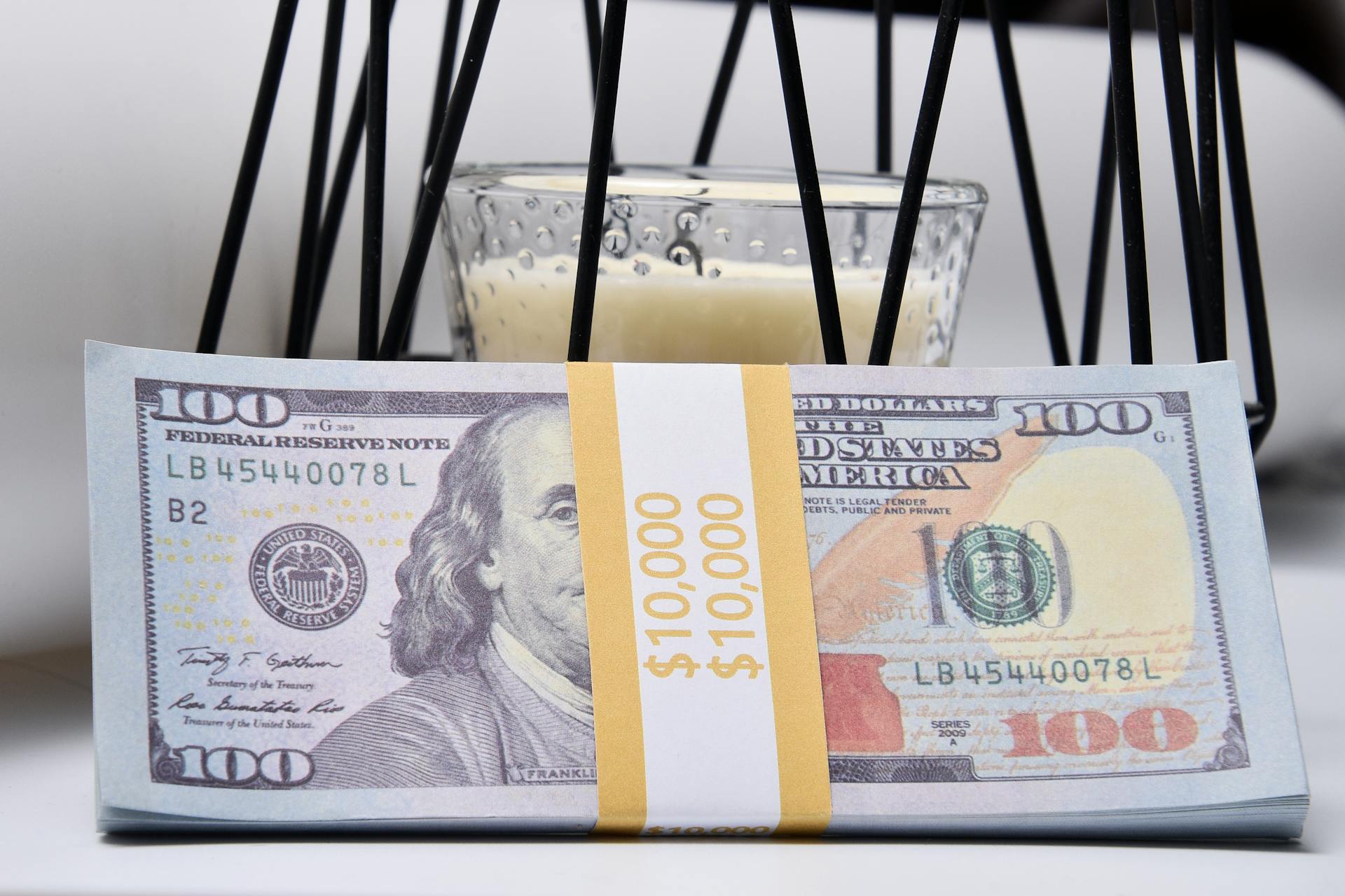 A stack of US dollar bills secured with a band, placed in front of a candle. Financial security concept.