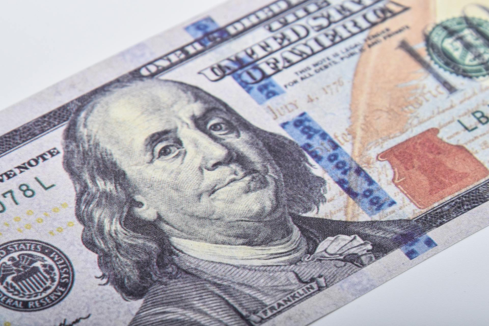 Macro shot of a US hundred dollar bill featuring Benjamin Franklin on a white surface.