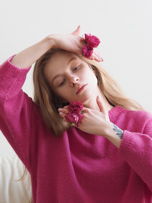 Free Portrait of Woman in Pink Sweater Holding Pink Flowers In-between her Fingers Stock Photo