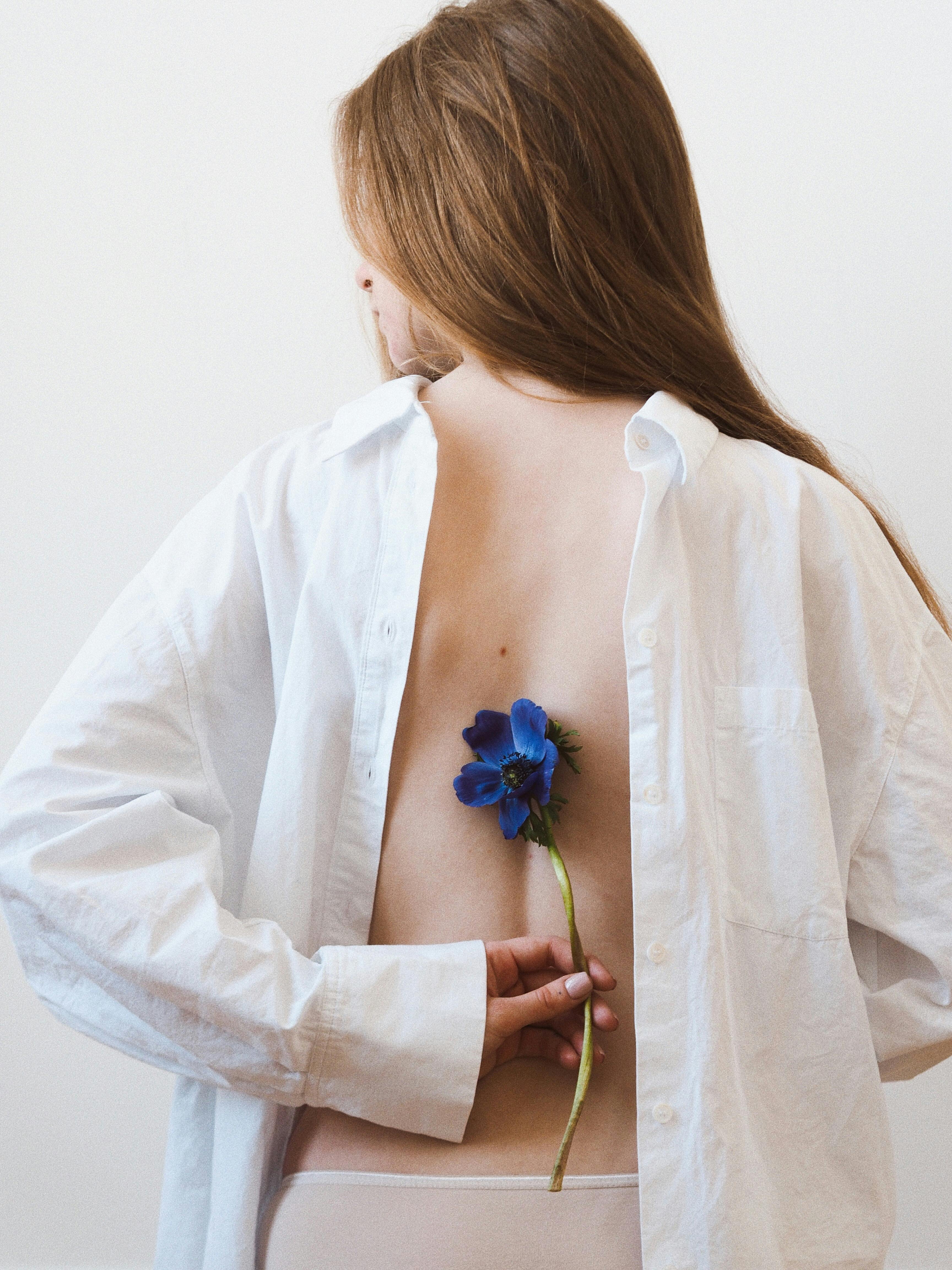 A woman in a white shirt holds a blue flower behind her back, adding a touch of elegance.
