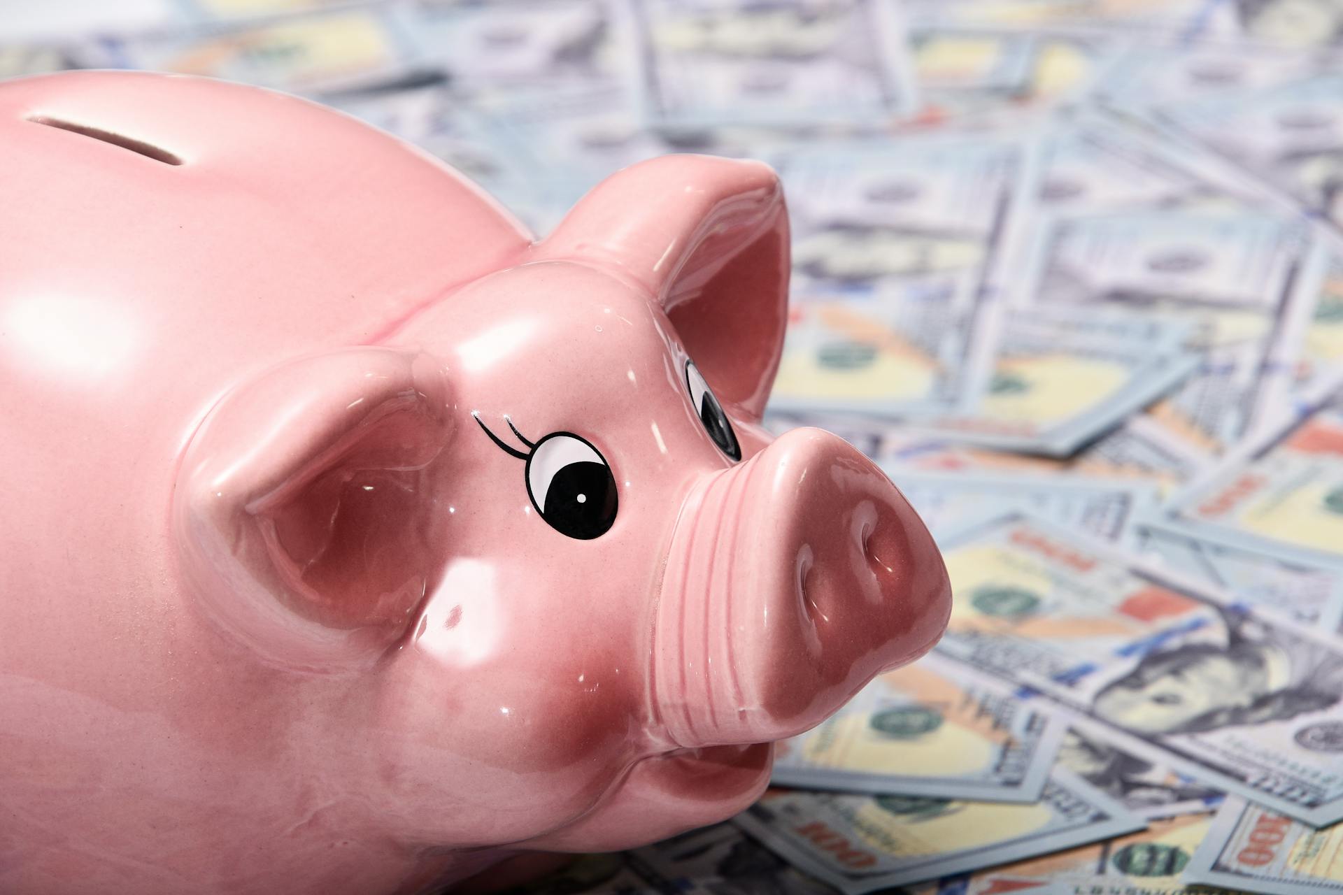 Close-up image of a shiny pink piggy bank surrounded by US hundred dollar bills, symbolizing savings and finance.