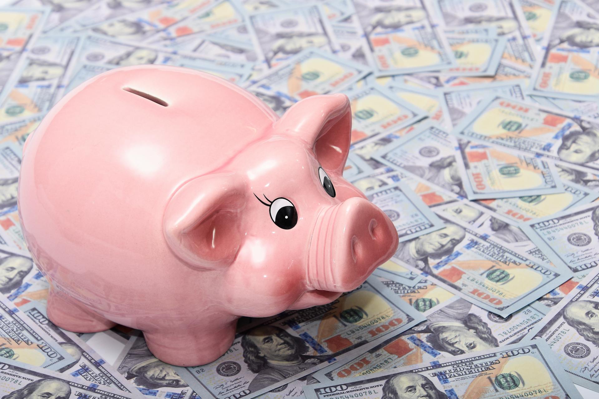 Pink ceramic piggy bank placed on a spread of US dollar bills symbolizing savings and financial security.