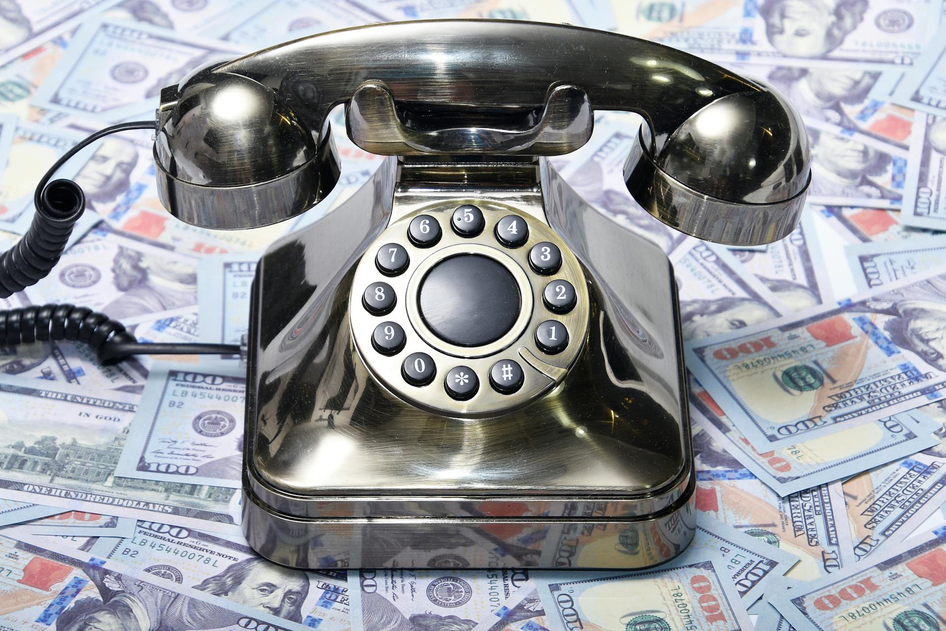 A retro rotary phone placed on a pile of US dollar bills, symbolizing communication and finance.