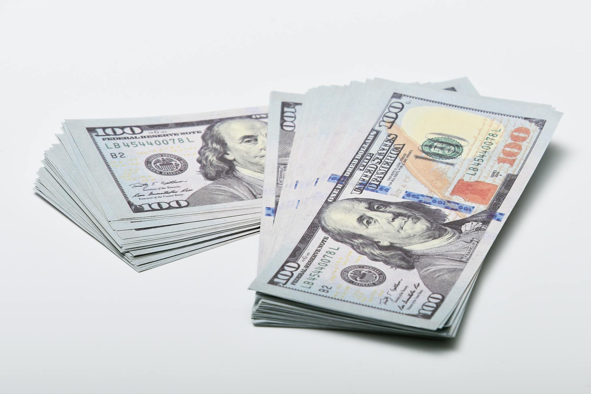 Close-up of two stacks of $100 US dollar bills on a white surface, showcasing currency and finance concepts.