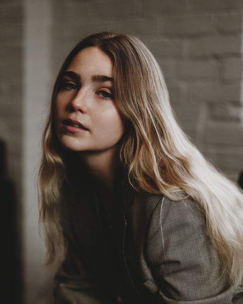 Free Artistic portrait of a young woman with long blonde hair and a neutral expression. Stock Photo
