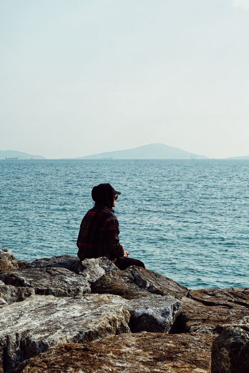 Free A person in a hat sits on coastal rocks, gazing at the sea in Istanbul, Turkey. Stock Photo