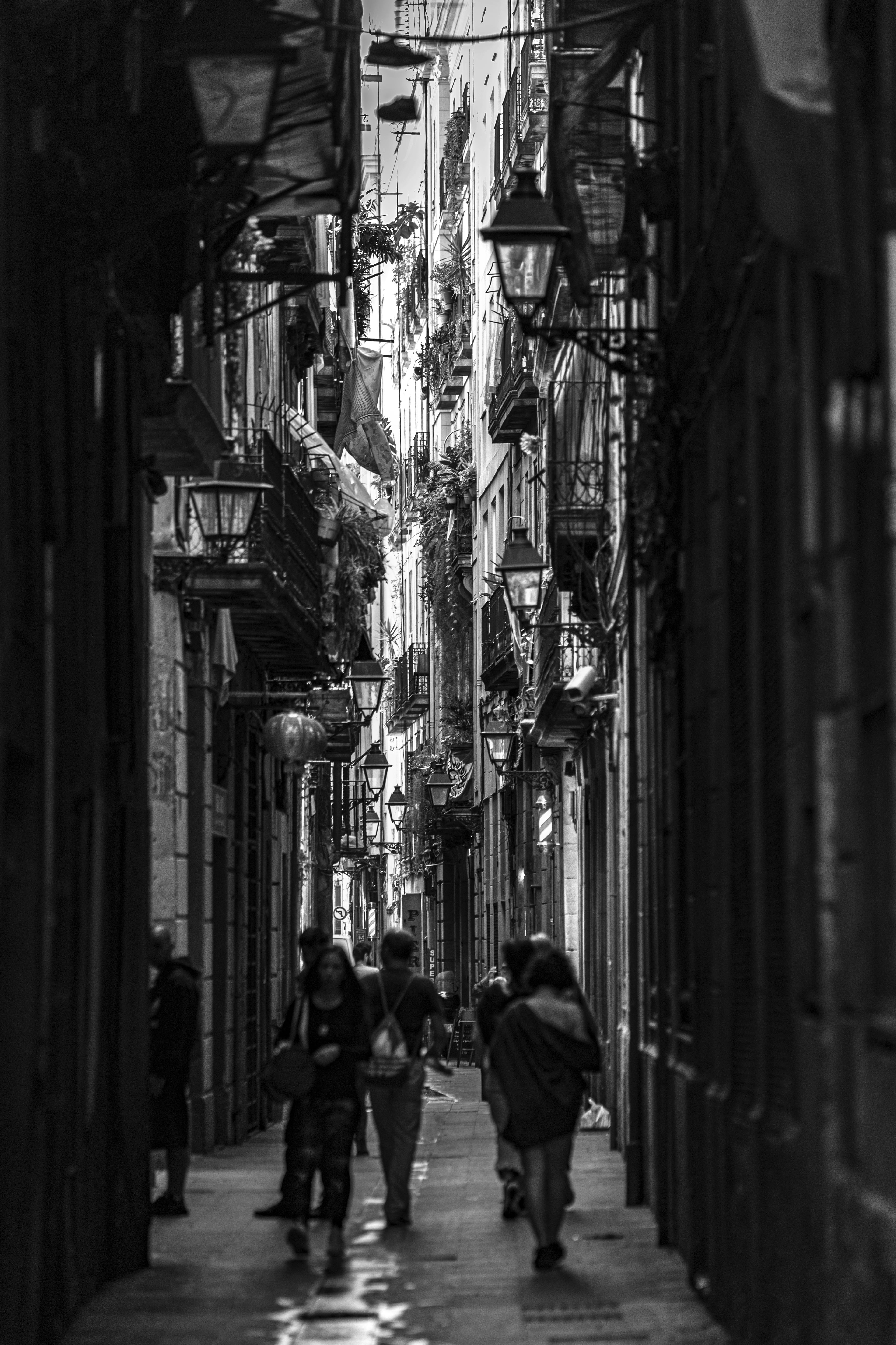 black and white photo of people walking in a alley in spain