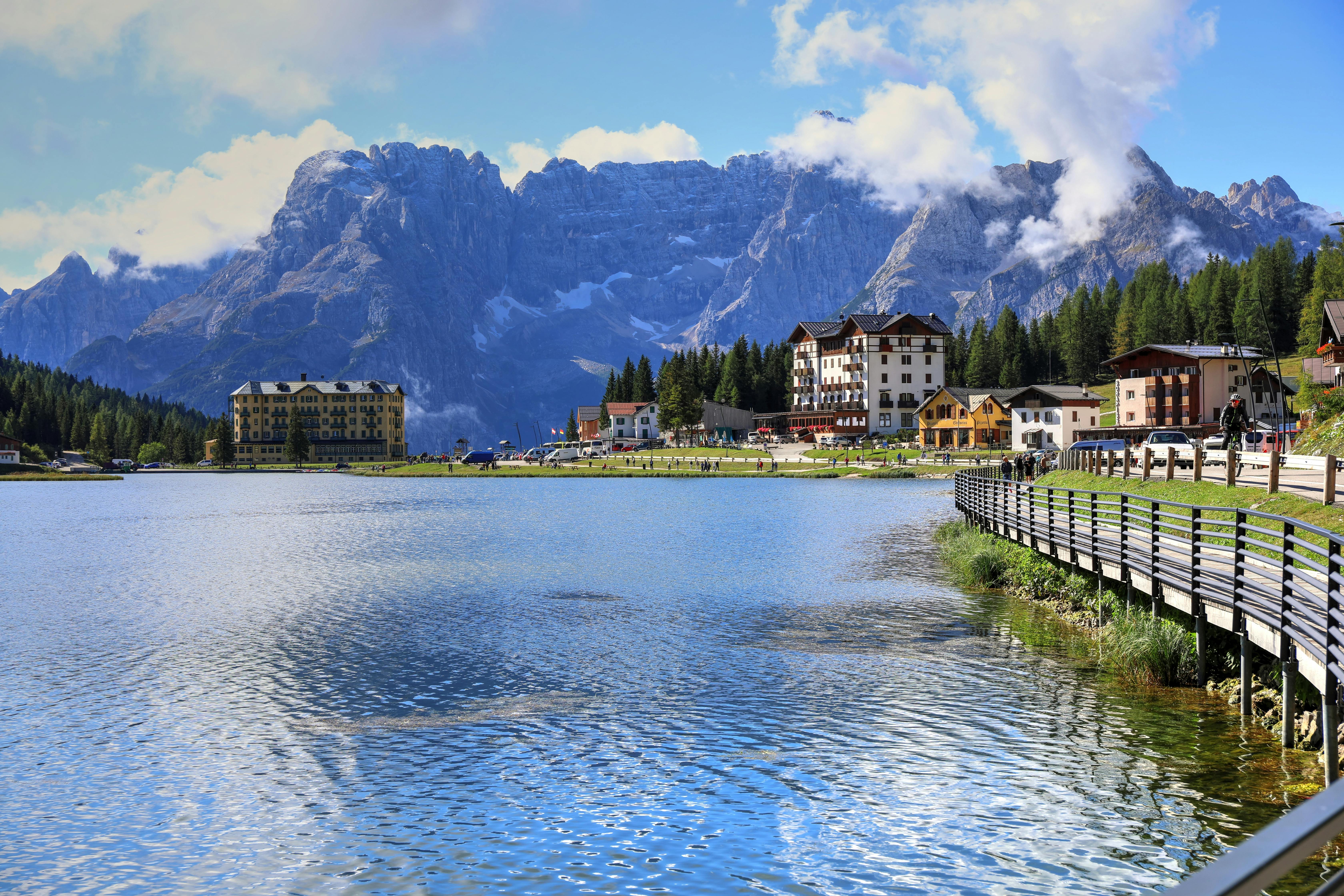Sunrise over Auronzo di Cadore in the Dolomites, golden light illuminating alpine meadows with traditional villages and Tre Cime peaks at dawn