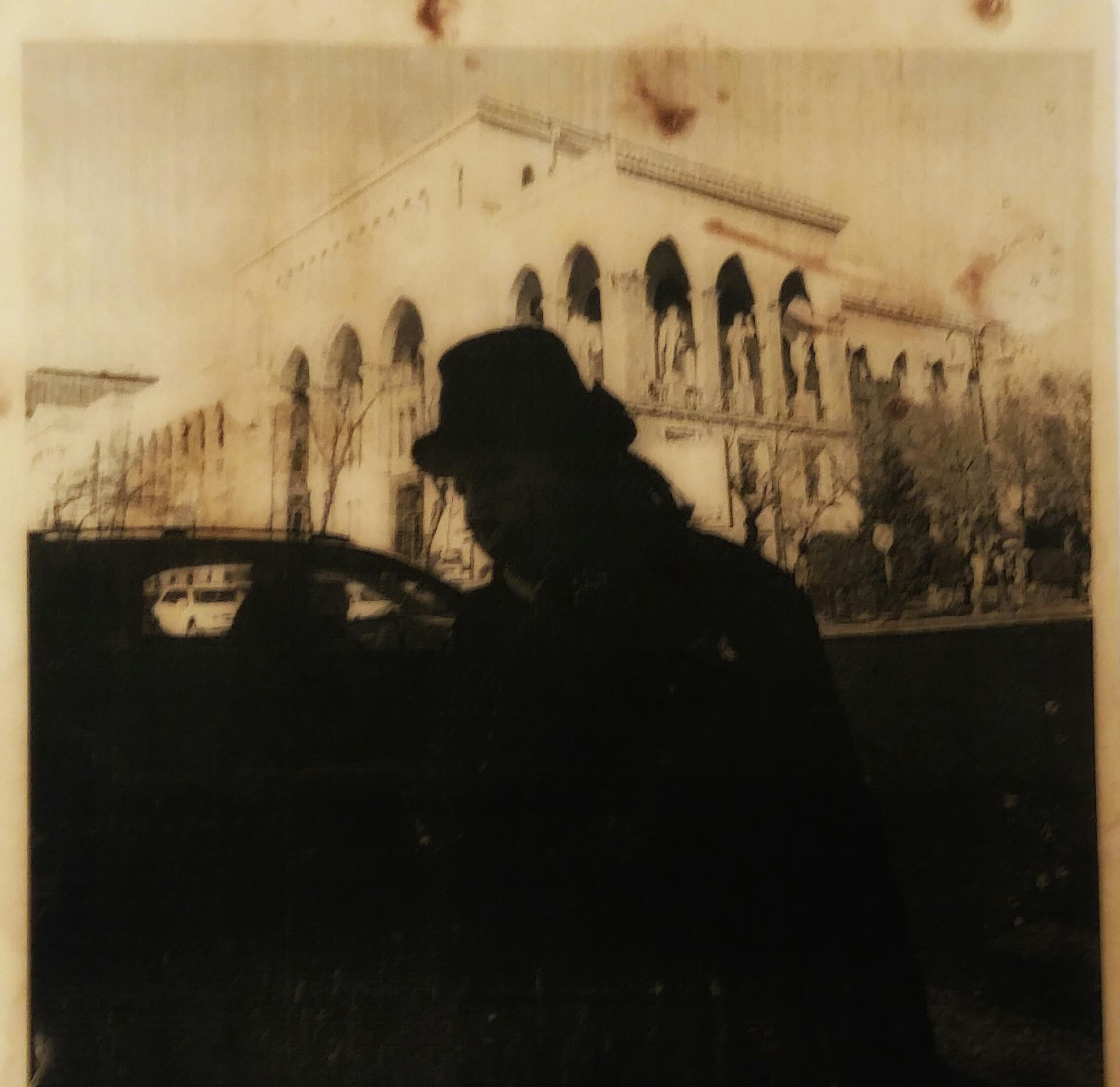 A sepia-toned image of a silhouette in front of classical architecture with vintage cars.