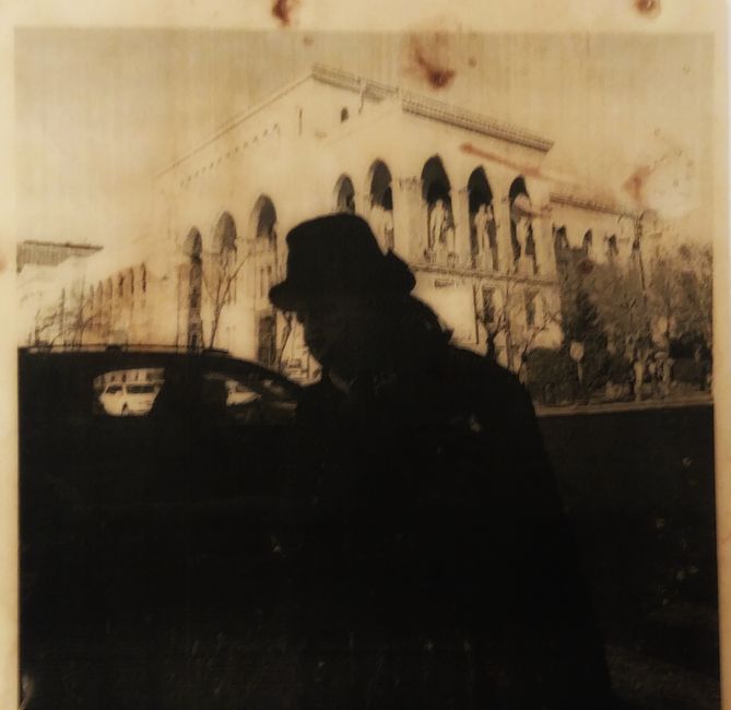 A sepia-toned image of a silhouette in front of classical architecture with vintage cars.