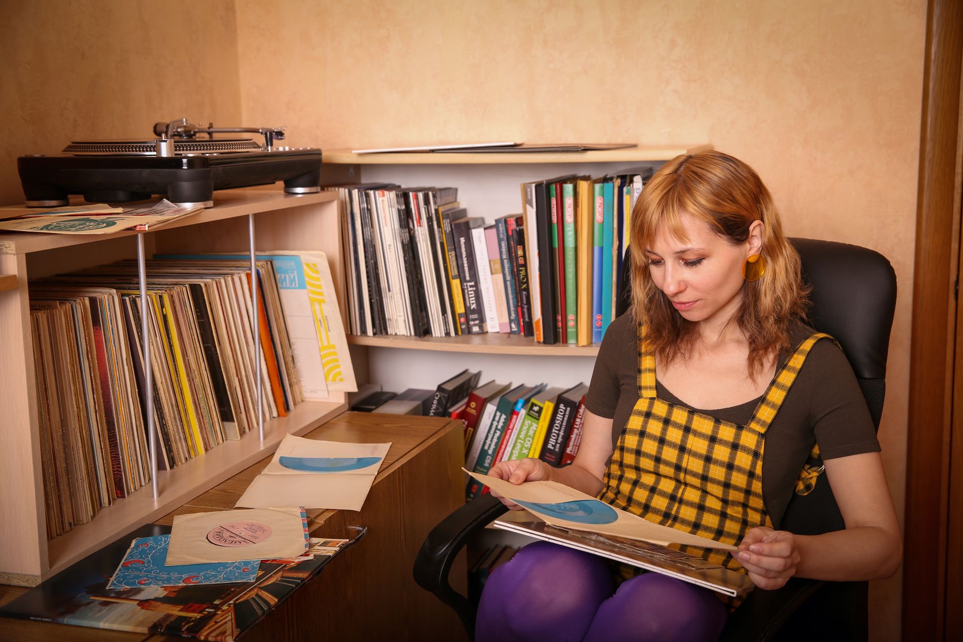 A woman browsing records beside bookshelves, absorbed in the slower work of choosing