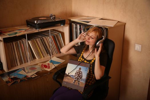 Woman sitting with headphones, surrounded by vinyl records, enjoying music in a vintage setting.