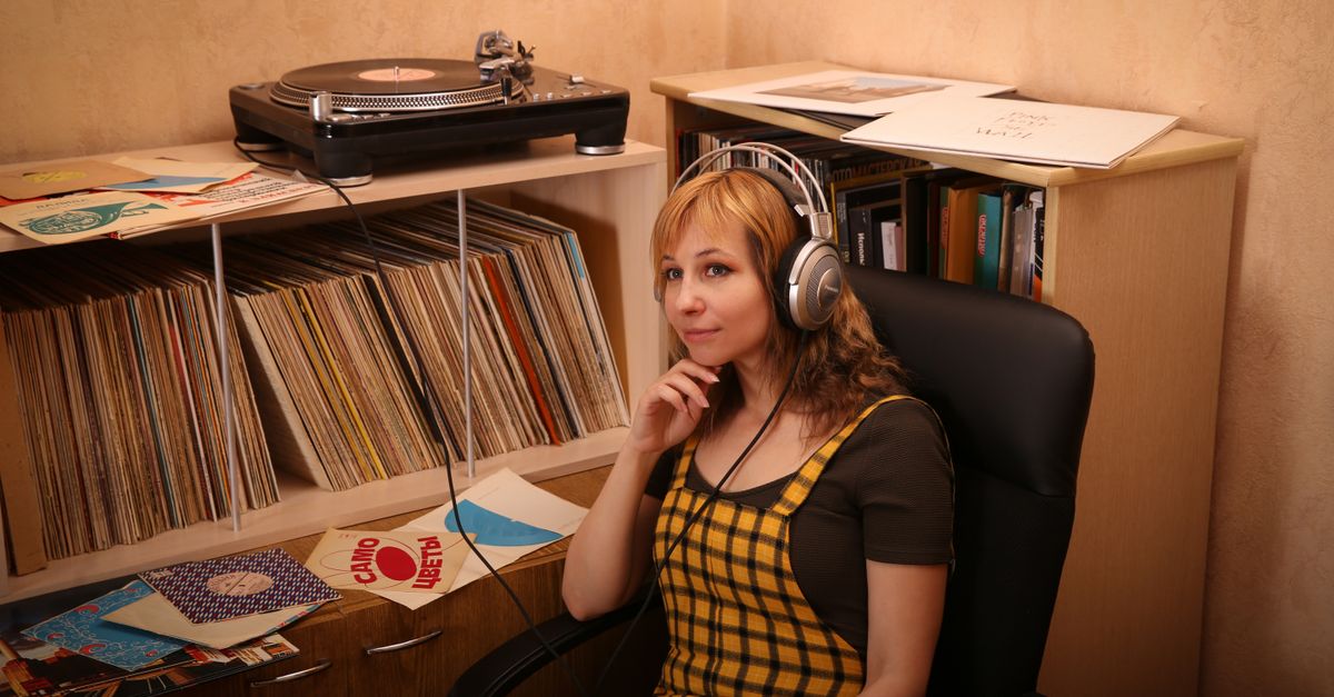 A person wearing headphones, looking at a vinyl record collection in a dimly lit room, with a focused expression