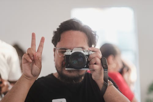 Man Doing Peace Sign While Taking Photo with a Camera