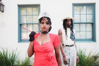 Woman in Elegant Red Dress Holding Cigarillos and Man with Dreadlocks Standing Behind