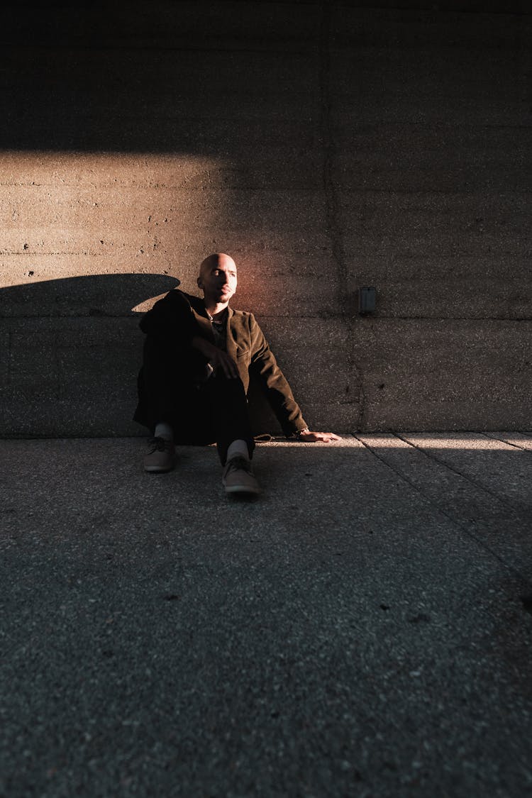 Bald Man Sitting On Ground And Leaning Against Concrete Wall