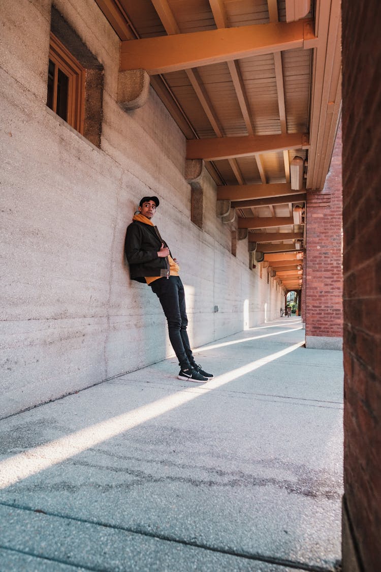 Man In Black Cap Leaning Against Concrete Wall Of Long Building