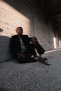 Bald Man Sitting Casually on Ground at Long Concrete Wall