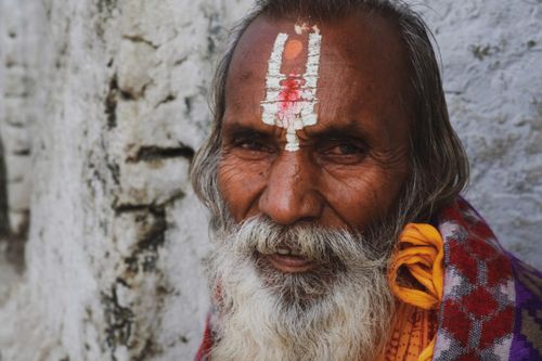 Free Close-up of an elderly man with gray hair and a tilak, against a textured wall. Stock Photo