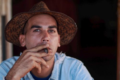 Free Close-up portrait of a man wearing a hat smoking a cigar, exuding a contemplative mood. Stock Photo