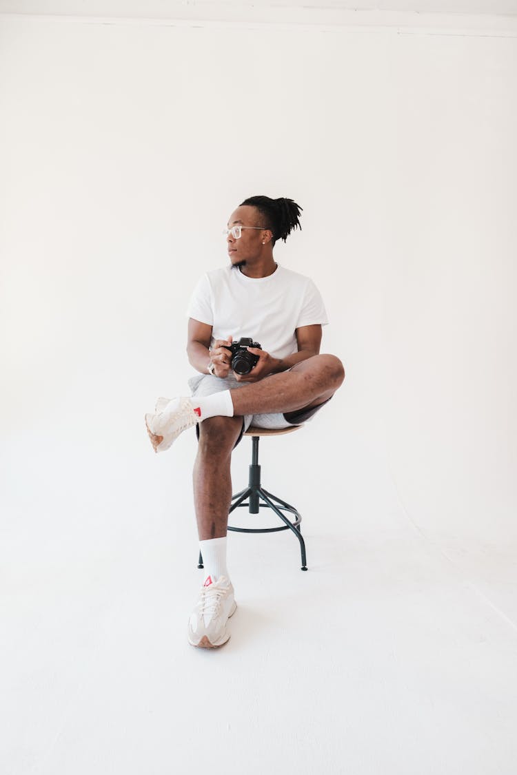 Man Sitting On Stool While Holding A Camera