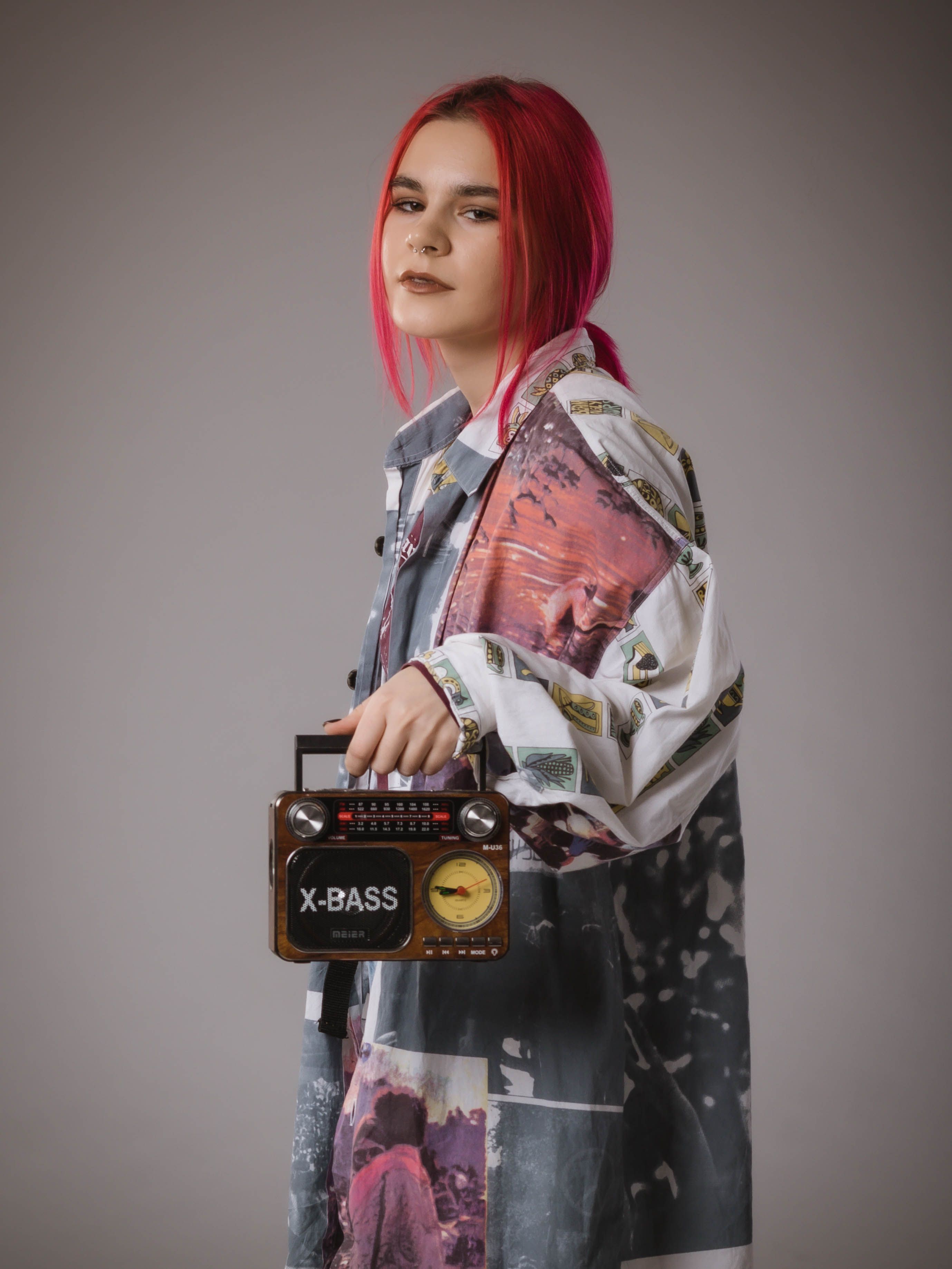 A fashionable woman with red hair holding a vintage-style portable radio against a grey background.