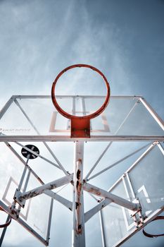 Rustic basketball hoop with metal frame shot from below against clear sky, emphasizing urban sports culture.