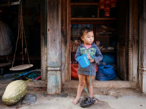 Free A young child stands in a rustic doorway holding a blue bucket, barefoot and curious. Stock Photo