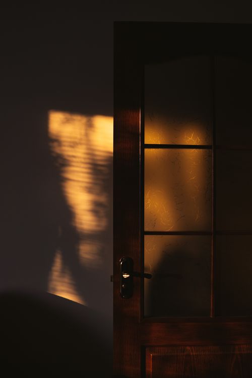 Free Golden sunlight creates dramatic shadows on a wooden glass-paneled door, enhancing its texture. Stock Photo