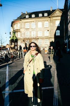 Confident woman in trench coat strolls through picturesque Copenhagen street, embracing the urban vibes.