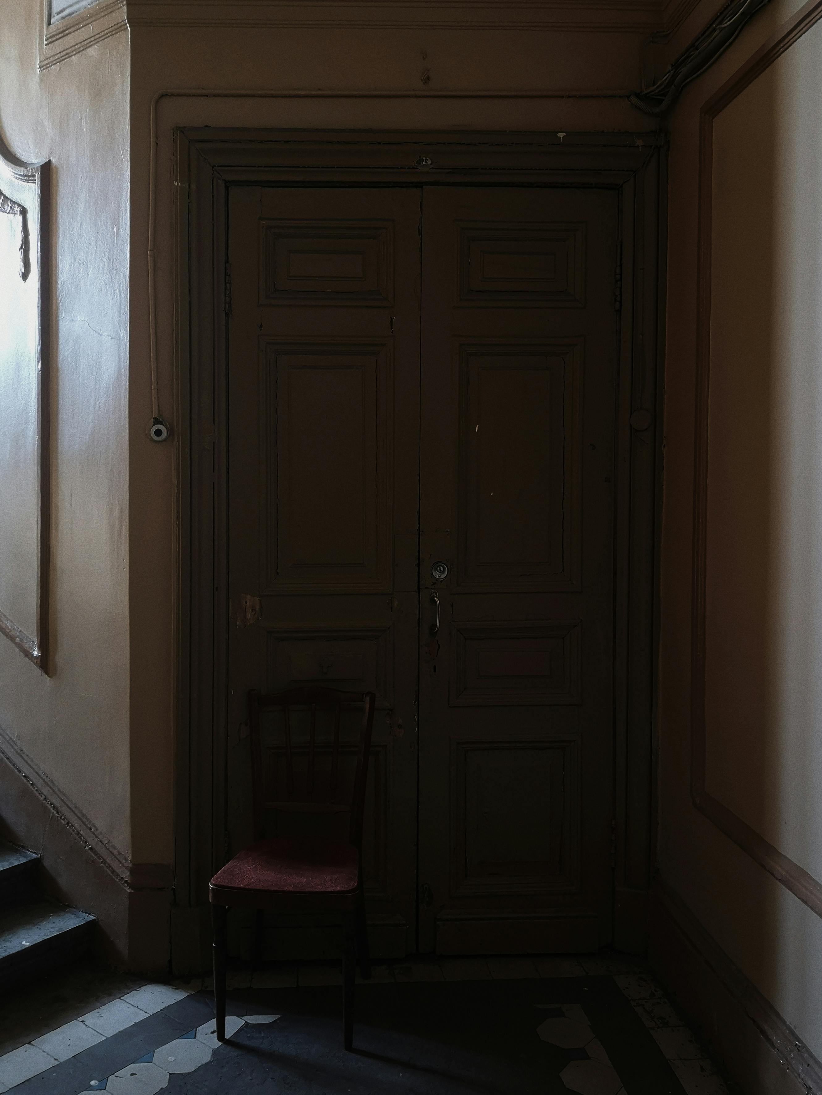 A dimly lit vintage wooden door with a chair in an old hallway, perfect for atmospheric themes.