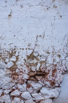 Detailed texture of a cracked and weathered wall with white plaster and exposed stones.