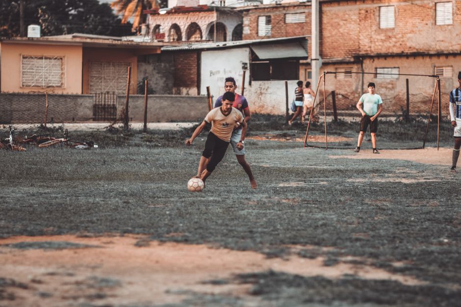 A group of men playing soccer on a makeshift field in an urban neighborhood.