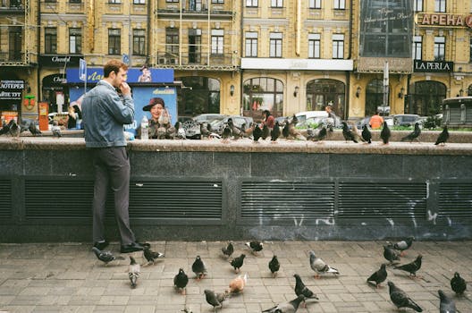 A man in a denim jacket stands in Kyiv surrounded by pigeons. Urban and lively.