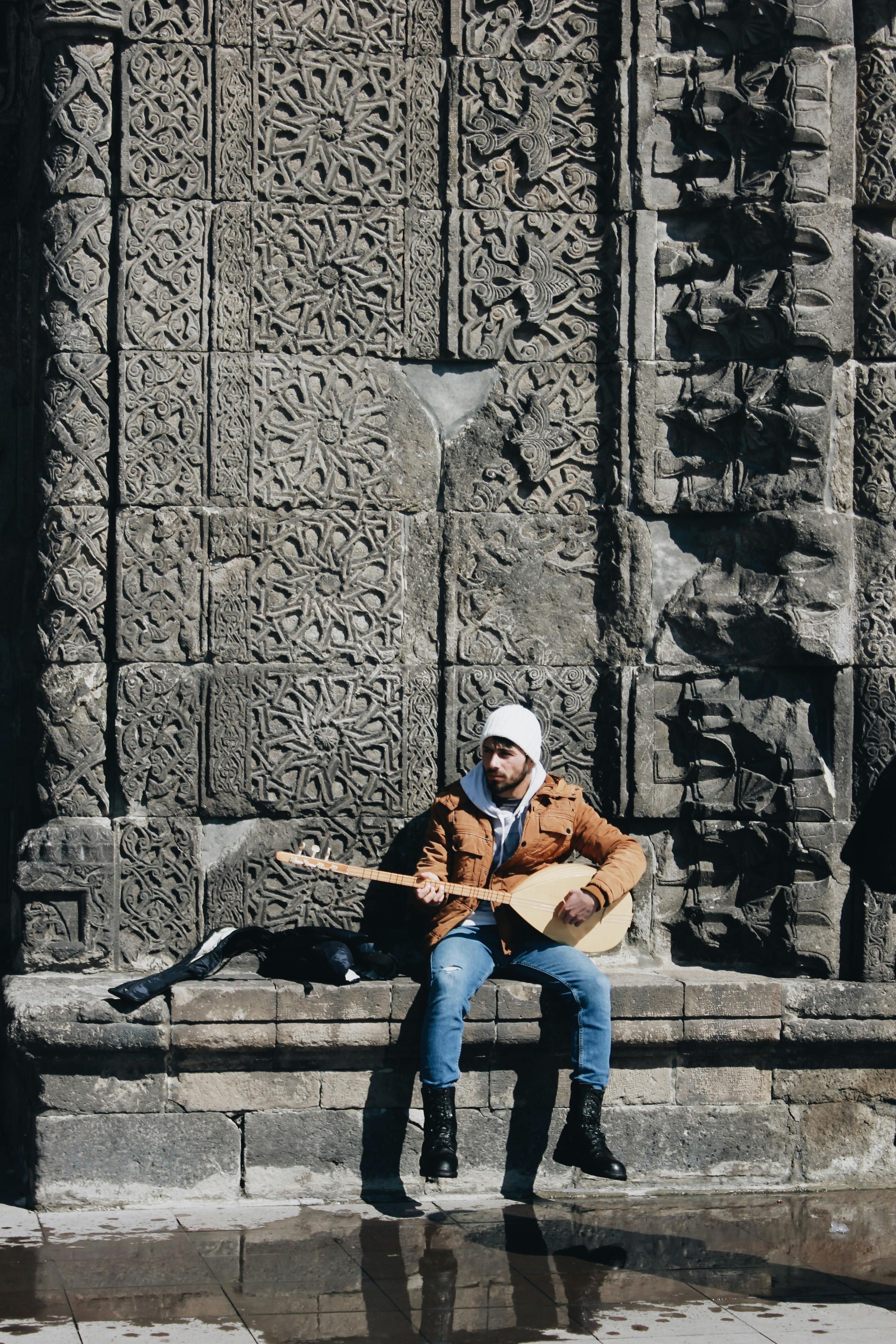 Man sitting on a Concrete Surface while Playing Stringed Instrument