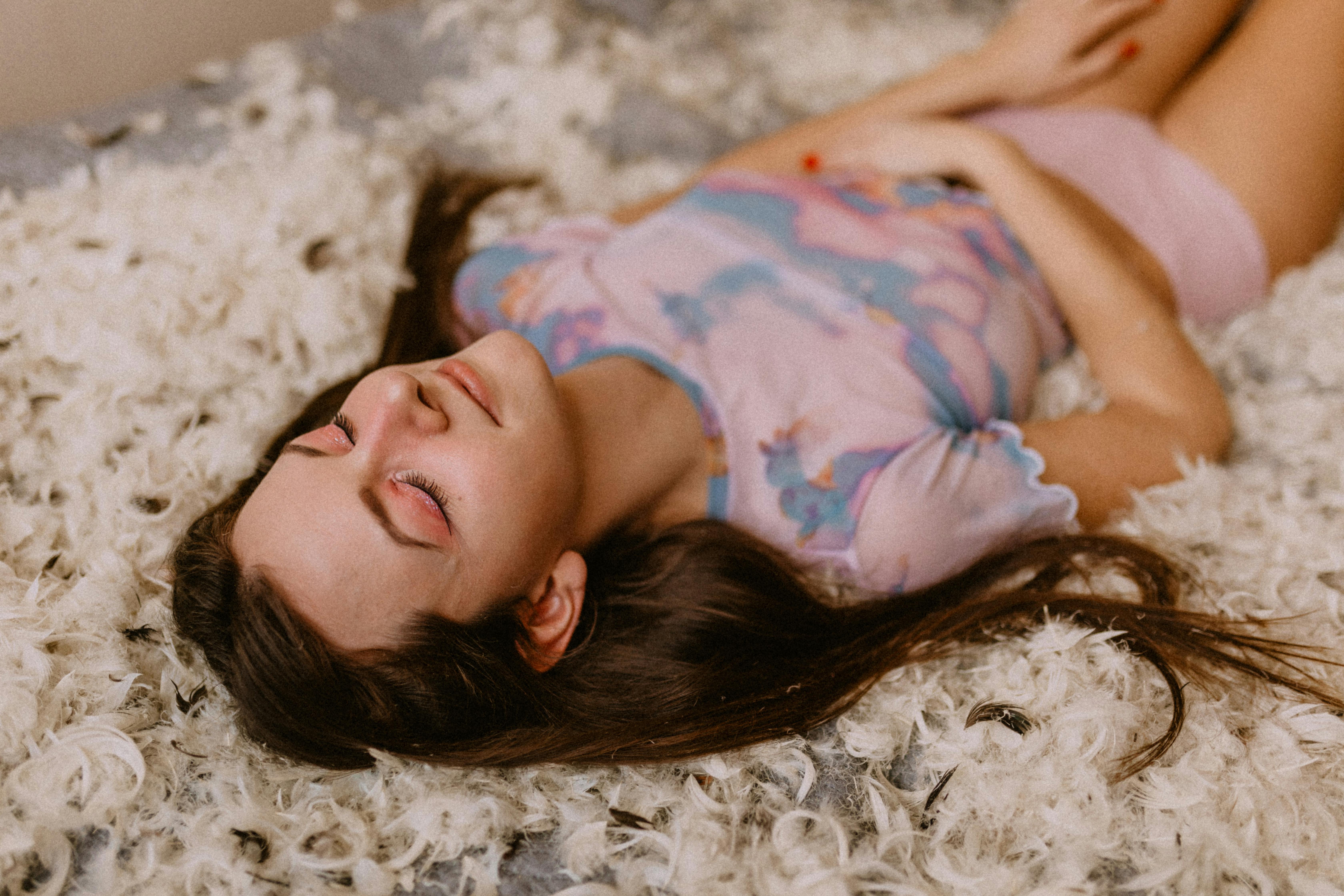 Beautiful woman lying peacefully on plush feathers, eyes closed in deep relaxation, embodying serene hypnotic surrender