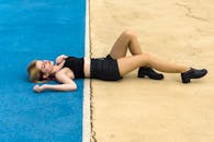 一名年轻女子身穿黑色服装，躺在户外蓝黄相间的人行道上