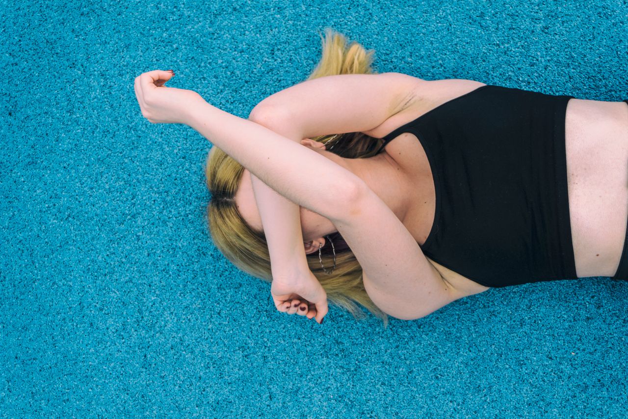 image of a young woman with blonde hair stretching on a vibrant blue s